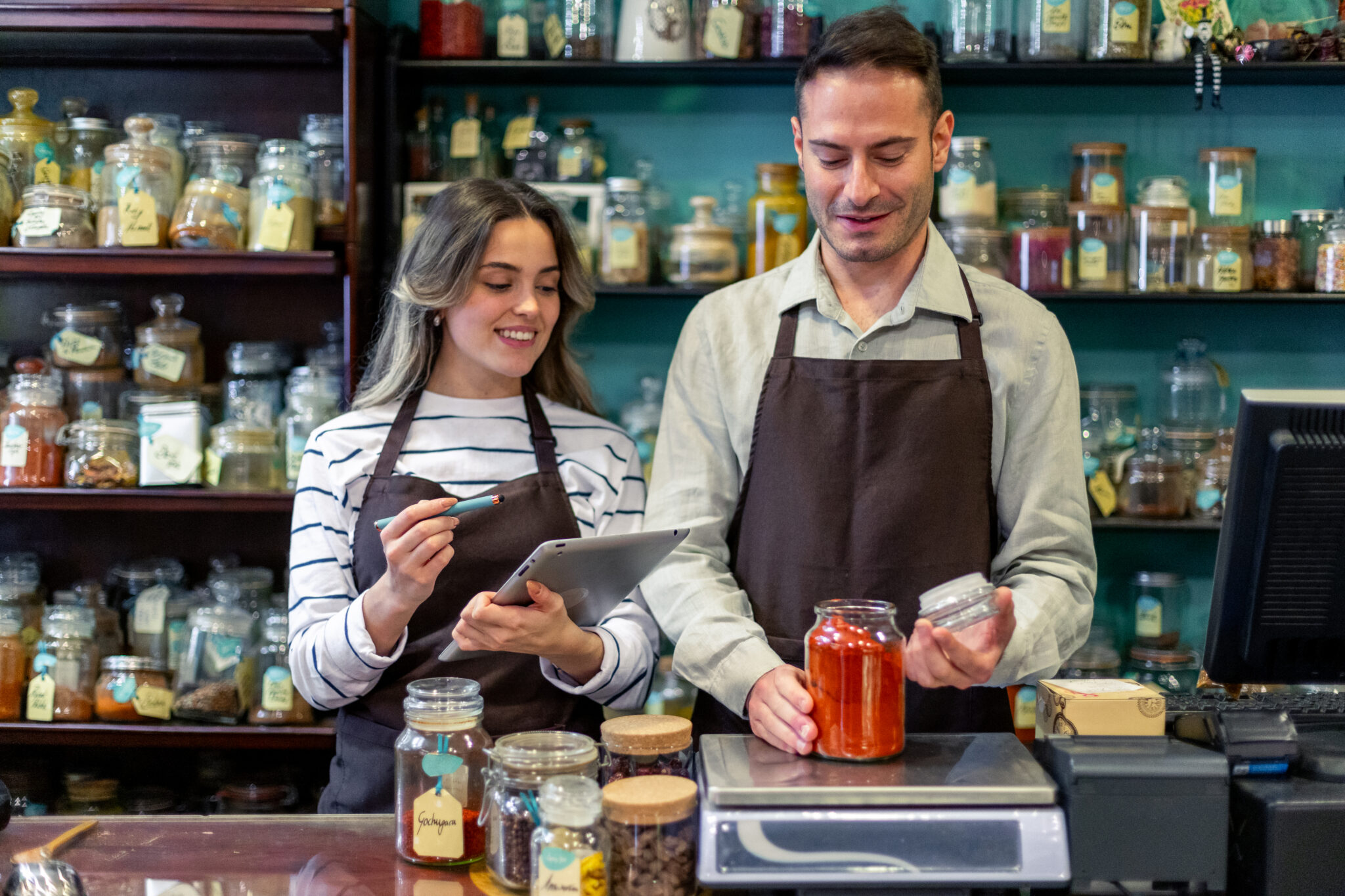 shopkeepers using digital tablet and weighing spices in jars at the counter